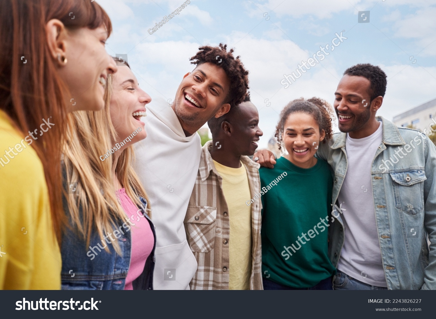 Young people walking laughing Happy friendship group of mixed race people cheerful together outdoors. Smiling students having fun during a travel trip. Multi-ethnic men and women hugging at the city #2243826227