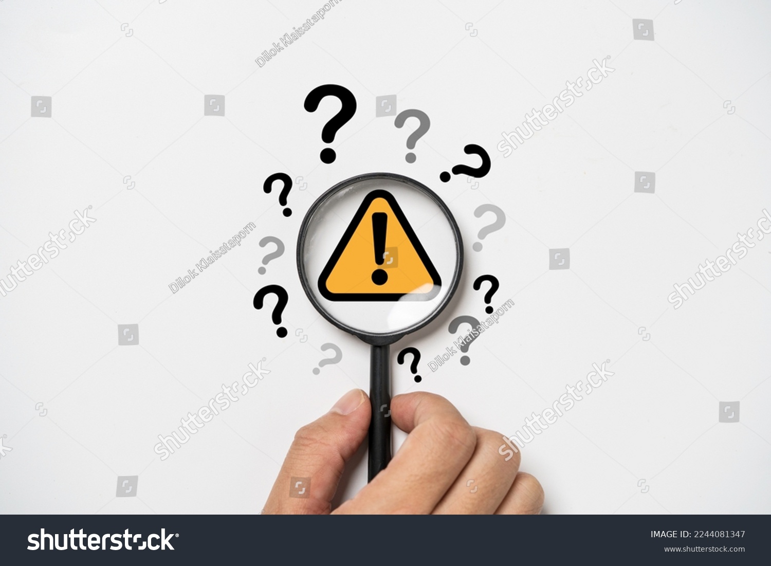 Hand holding magnifier glass with yellow triangle caution warning sign and question mark for notification error and maintenance concept. #2244081347