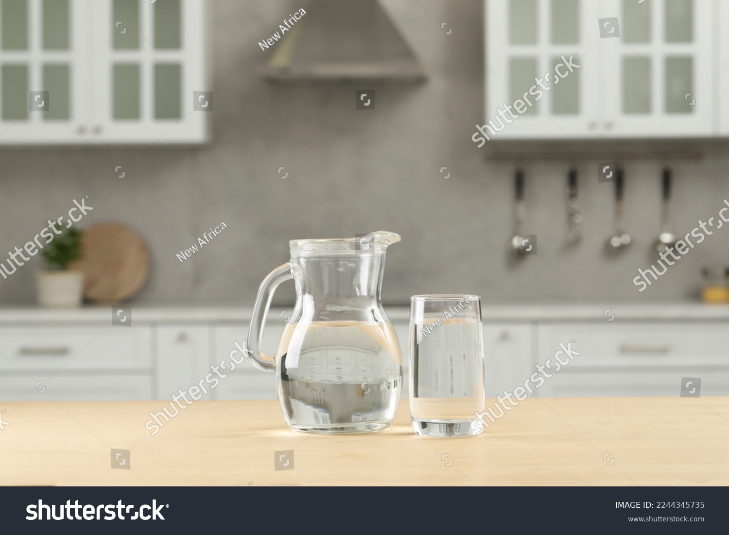 Glass and jug with water on wooden table in kitchen #2244345735