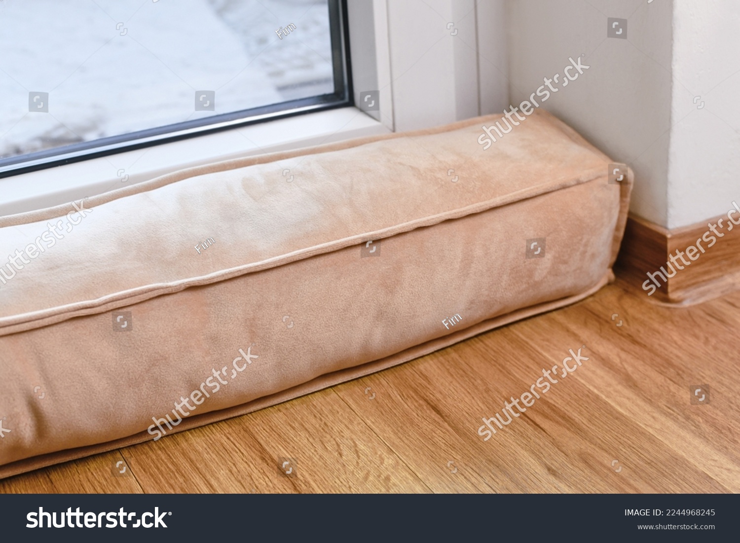 Draft excluder lying in front of door to keep out cold air and save energy for heating in room #2244968245