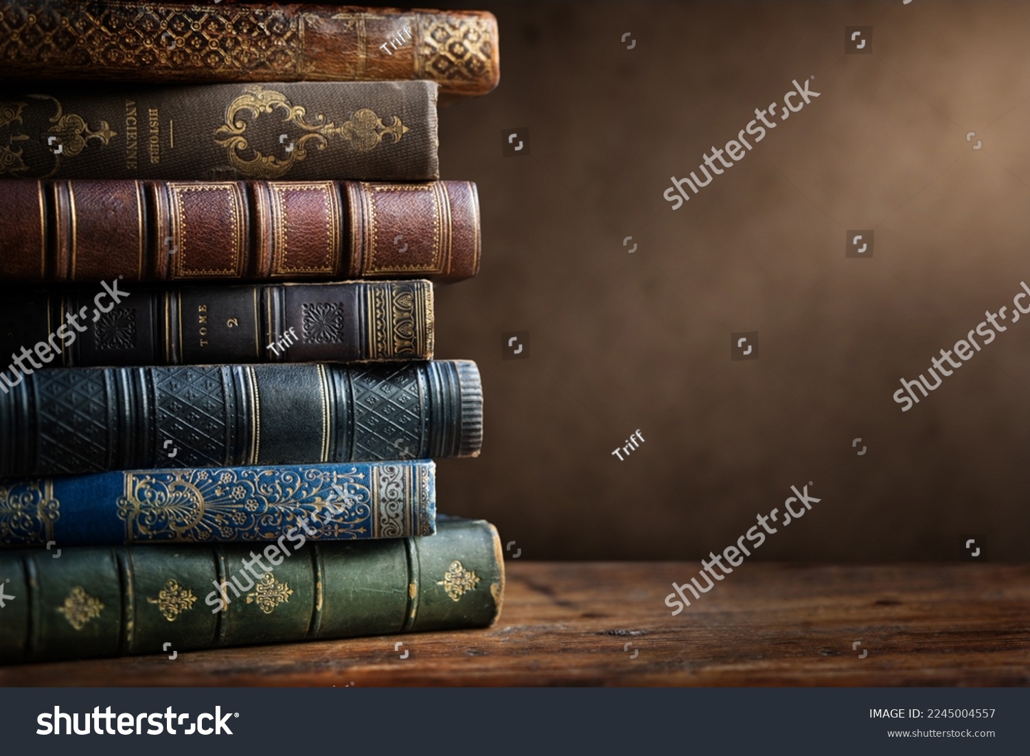 Old books on wooden desk and ray of light. Bookshelf history theme grunge background. Concept on the theme of history, nostalgia, old age. Retro style. Old book as a symbol of knowledge. #2245004557