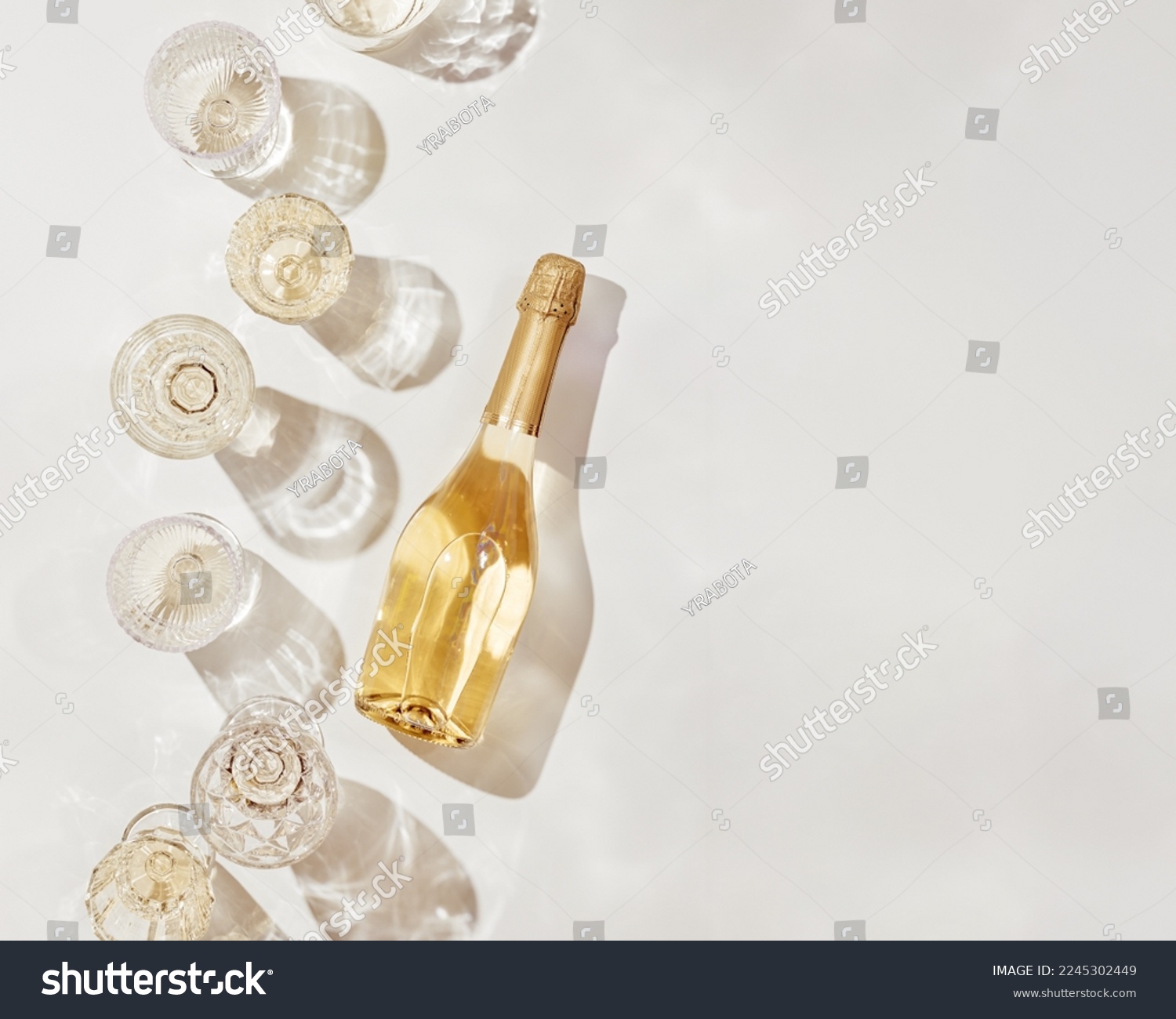 Flat lay with white sparkling wine bottle, set glasses wine with sunshine shadow and flare on light beige background. White wine aesthetic photo, copyspace. Summer holiday monochrome color still life #2245302449