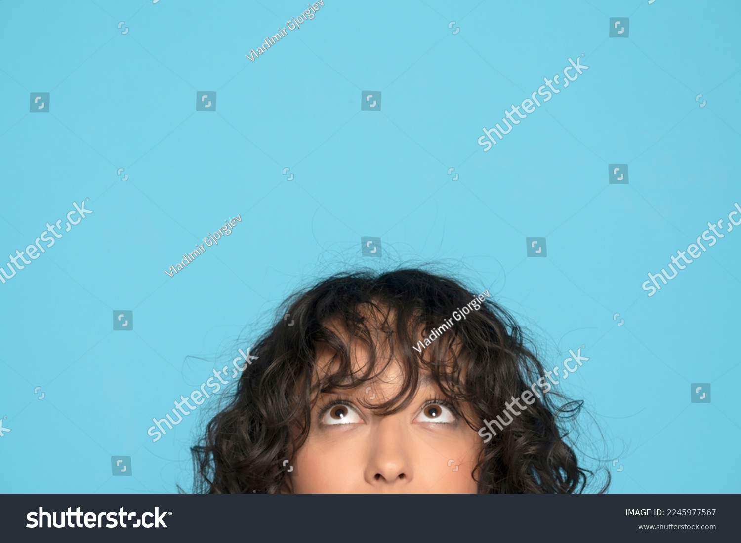 closeup portrait headshot cropped face above lips of cute happy woman looking up isolated on blue studio wall background with copy space above head. #2245977567