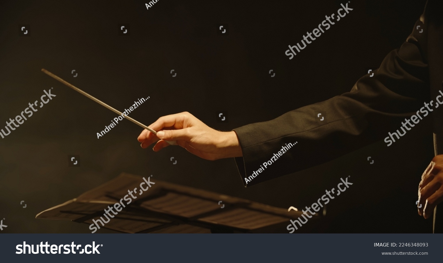 Close up shot of hands of symphony orchestra conductor directing music by waving his baton. Studio shot on black background  #2246348093