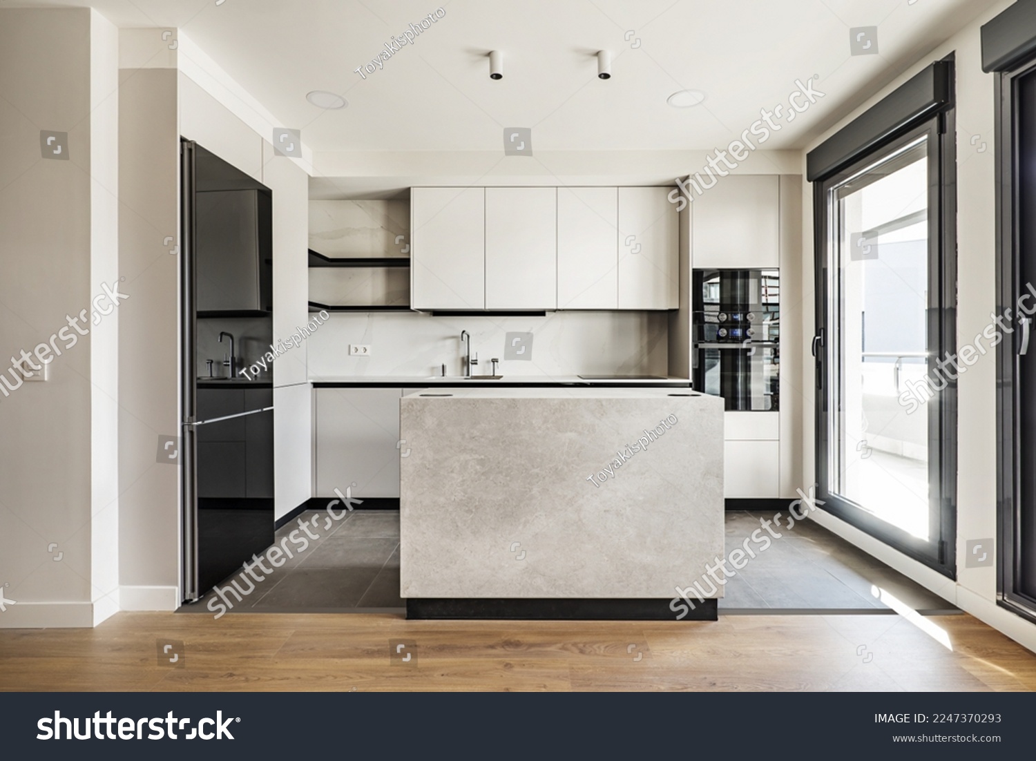 Front view of a modern designer kitchen with smooth handleless cabinets with black edges, black glass appliances, a marble island and marble countertops #2247370293