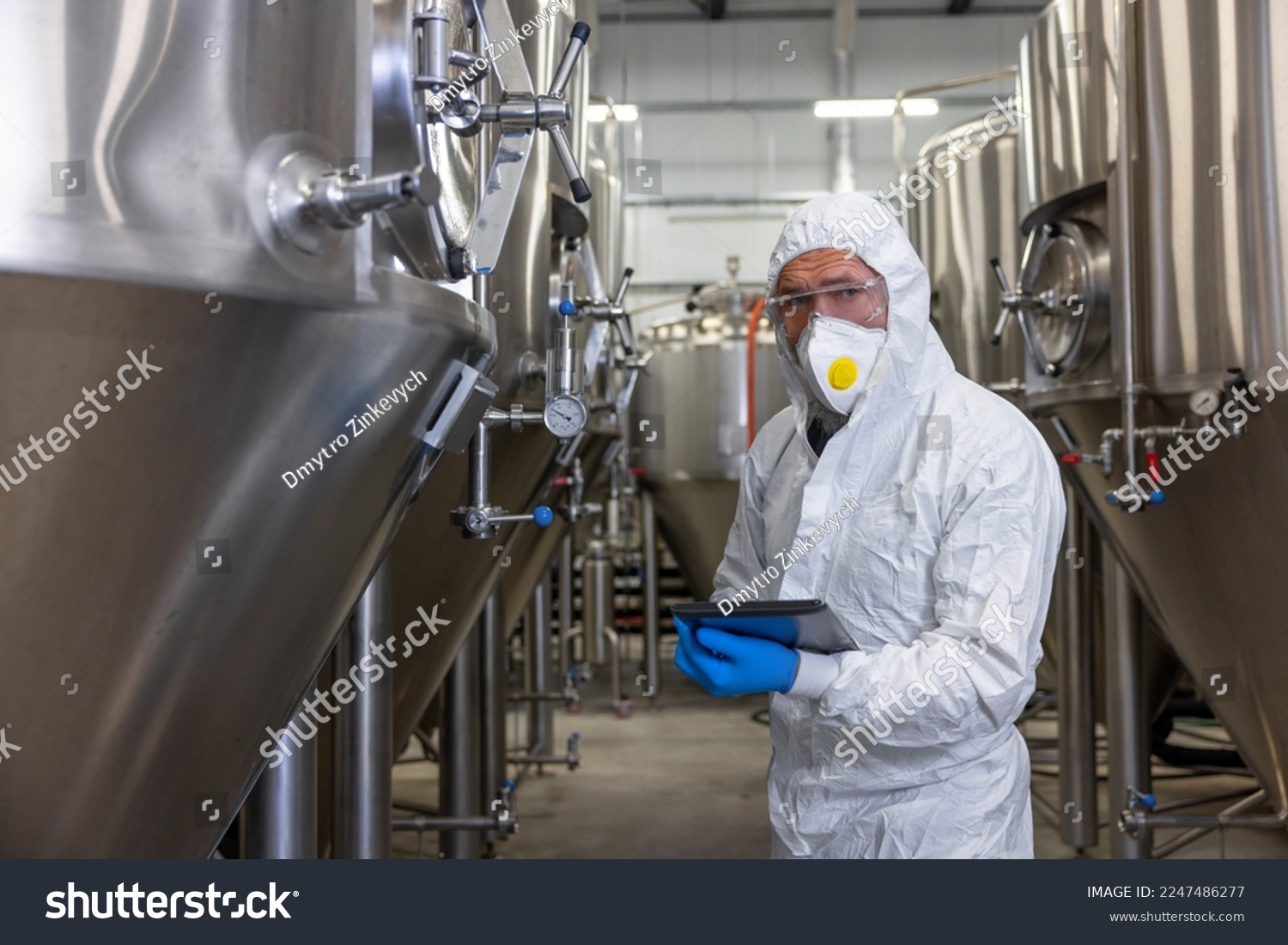 Experienced engineer overseeing the beer production equipment in a factory #2247486277