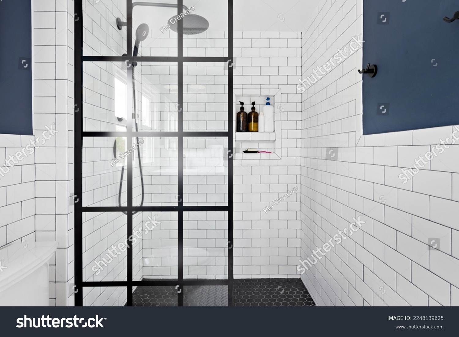 Styled Updated Bathroom Interior. Renovated white bathroom with contemporary design and modern fixtures. Glass enclosed shower with white subway tile and rainfall showerhead. #2248139625