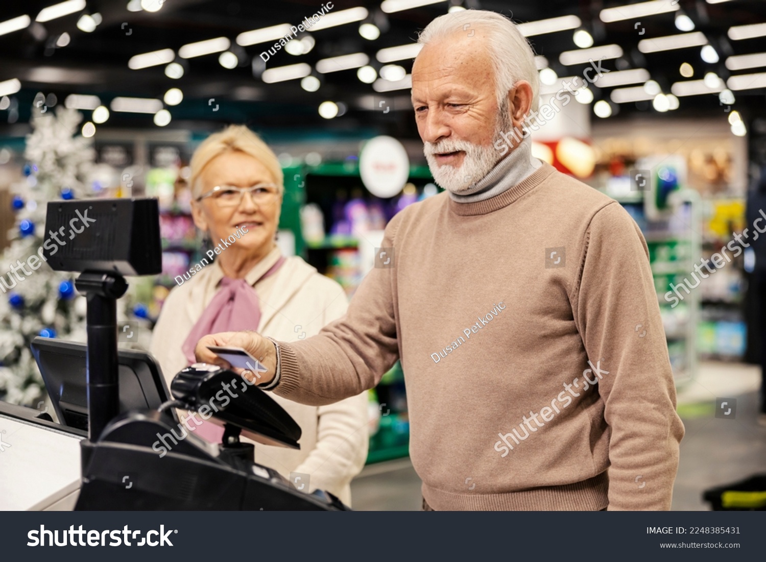 A senior man is paying with credit card on self-service cash register at the supermarket. #2248385431