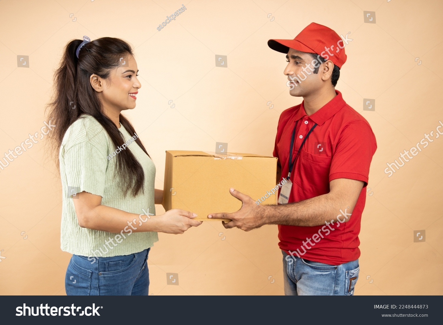 Indian Woman Receiving Box From Courier Man Standing Over Beige Studio Background. Post Package Delivering And Transportation, Couriers Service Concept. Parcel Delivery.Closeup Shot. #2248444873