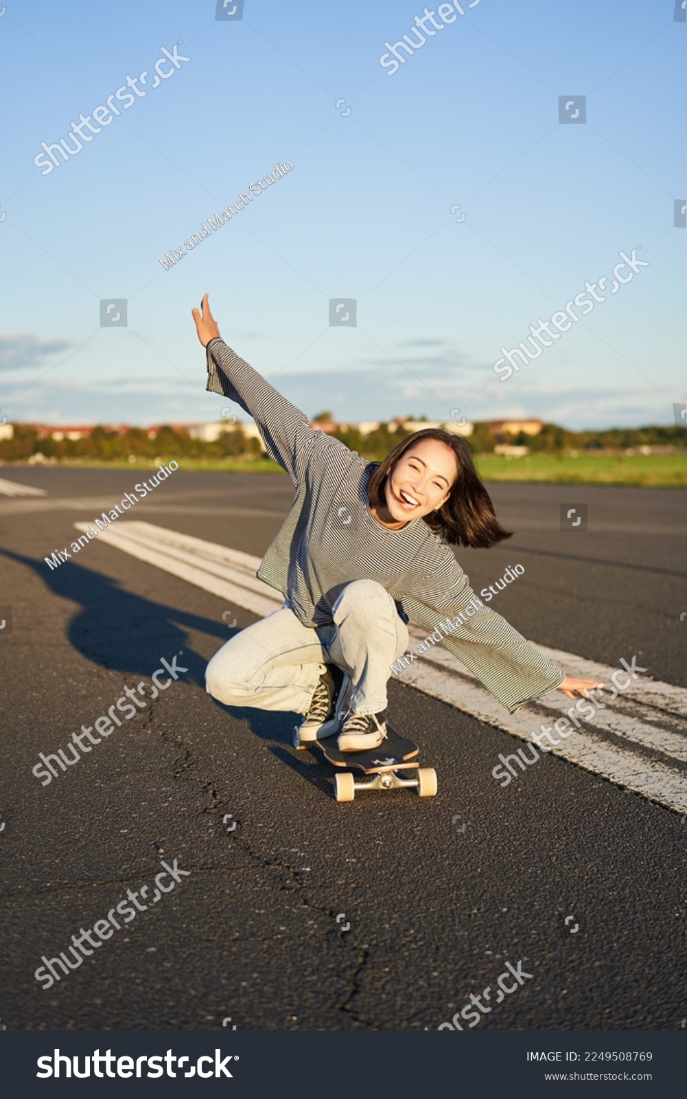 Carefree skater girl on her skateboard, riding longboard on an empty road, holding hands sideways and laughing. #2249508769