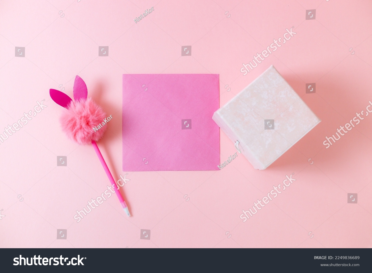 A gift box, a pink blank sheet, a pen with a fluffy head and bunny ears lie in the center on a pale pink background with copy space, flat close-up. Valentine's day concept. #2249836689