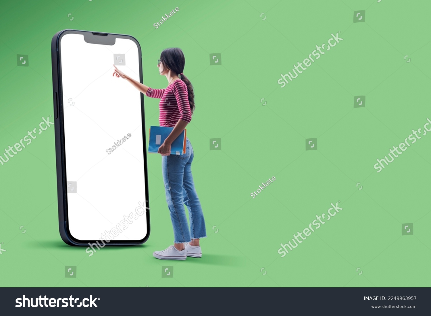 Female student holding notebooks and using a big smartphone with blank screen, e-learning concept, copy space #2249963957