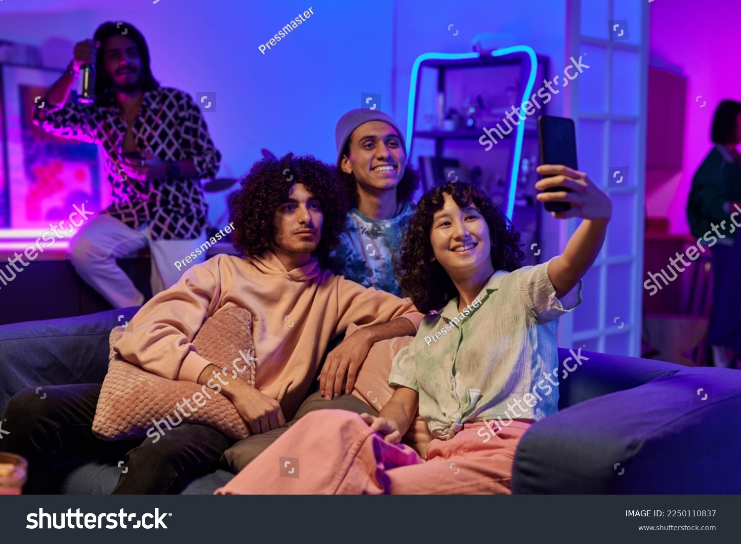 Happy youthful intercultural friends in casualwear taking selfie at home party while relaxing on comfortable couch in living room #2250110837