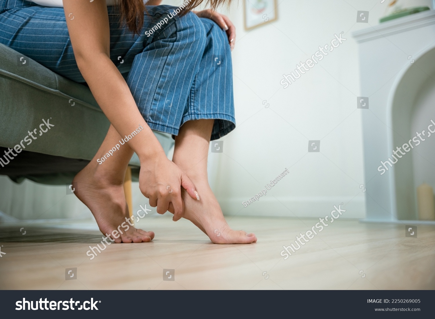 Asian young woman sitting on sofa holding her feet and stretch muscles have symptoms feeling pain, beautiful female problems with foot at home, painful ankle injury, Health care and medical concept #2250269005