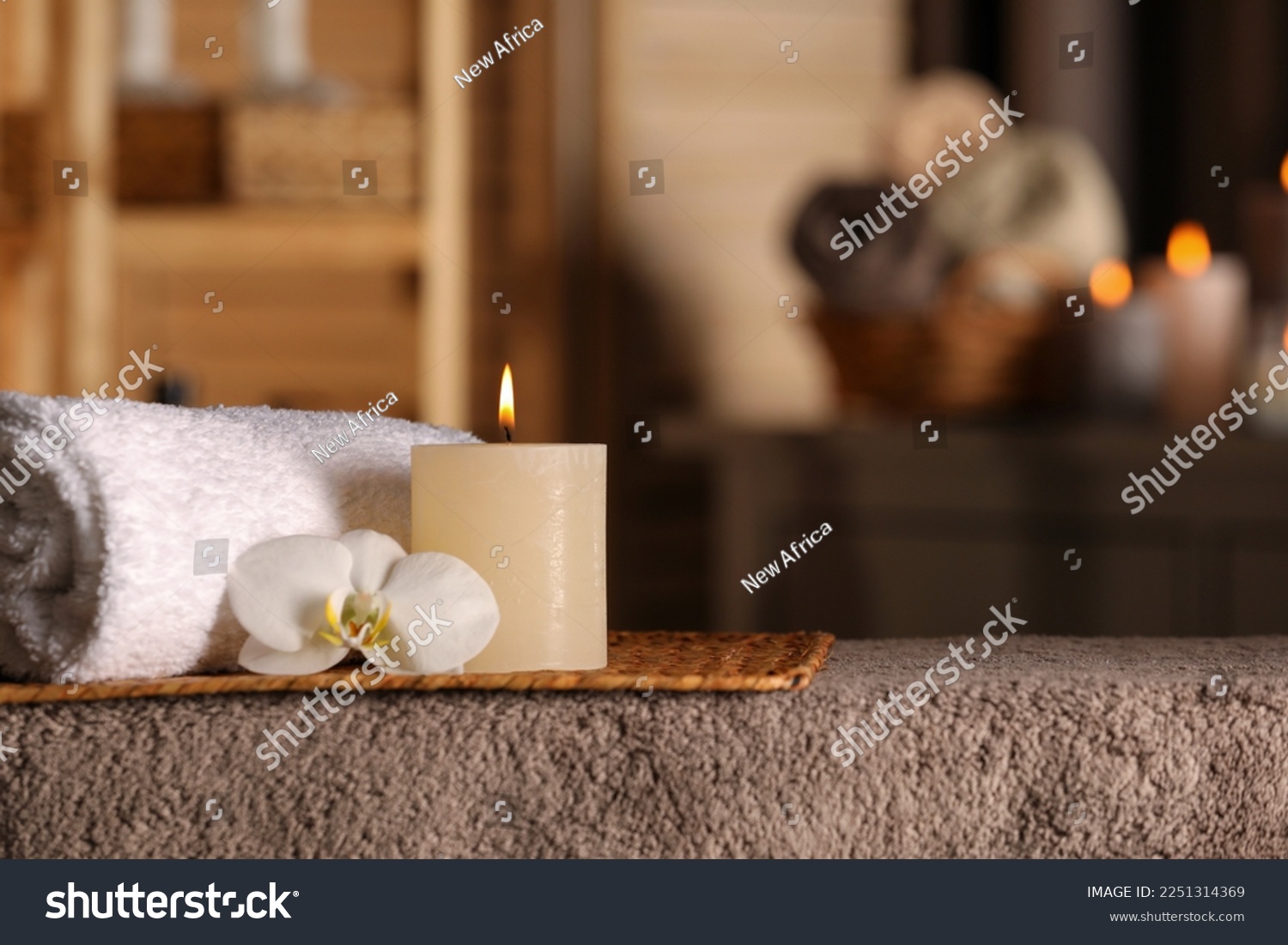 Spa composition with candle, orchid flower and rolled towel on massage table in wellness center, space for text #2251314369