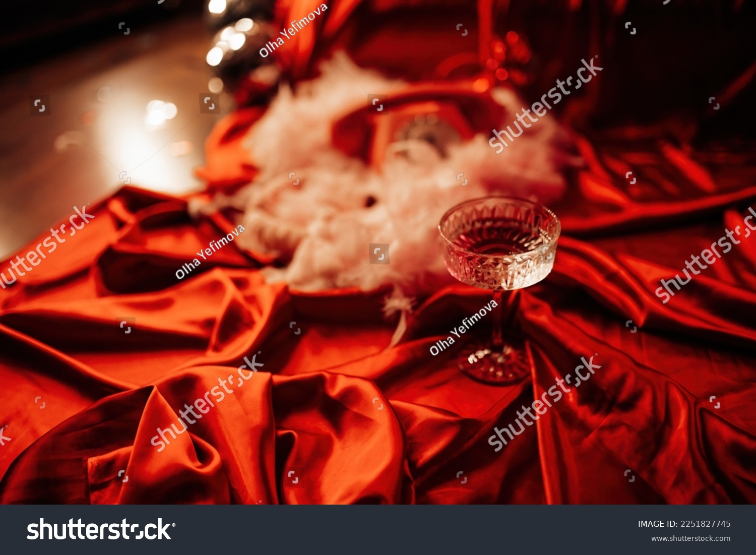 Extravagant glamour background with coupe glass of sparkly wine for love party at muffled light. Beautiful romantic burlesque place for st valentines holiday in red silk glossy sheets #2251827745
