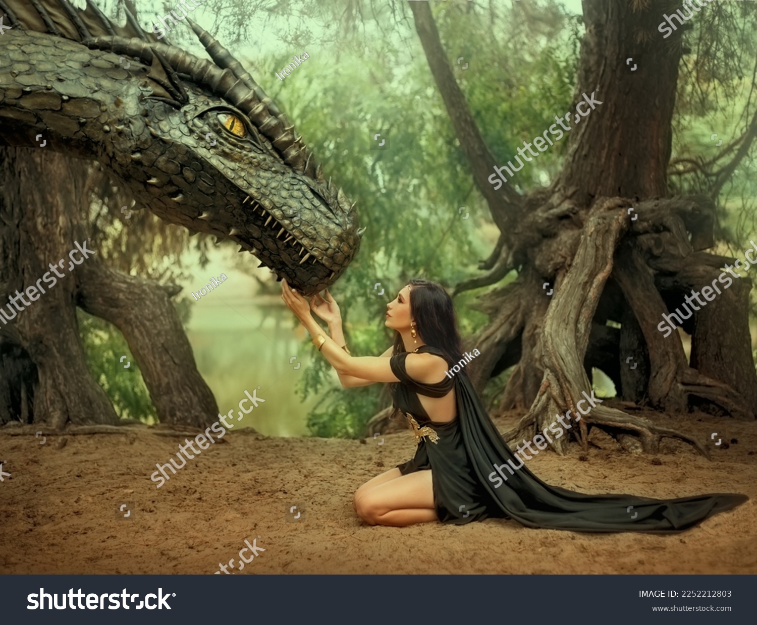 Fantasy woman elf queen touching with hands dragon head. Girl mistress tamed monster concept female power. black creative dress, girl princess fashion model sits on knees. Deep green forest trees. #2252212803