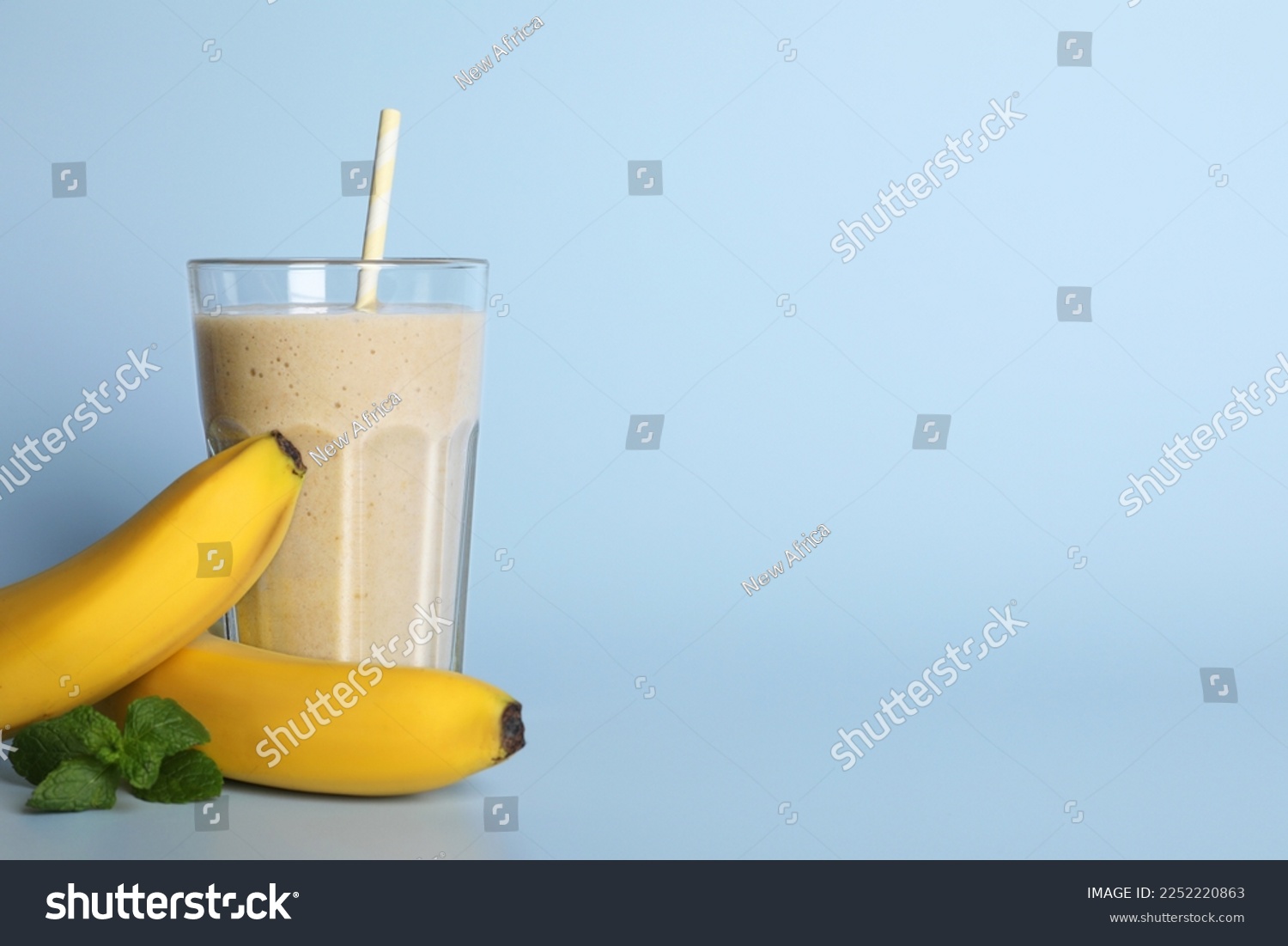 Glass of tasty smoothie with straw, bananas and mint leaves on light blue background. Space for text #2252220863