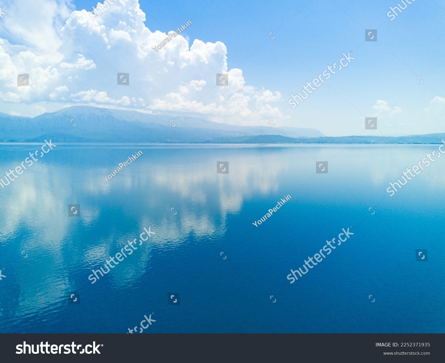 Majestic huge white thick clouds float across the clear blue daytime sky above the horizon with the shallow azure calm Adriatic Sea in the light of the bright summer sun #2252371935