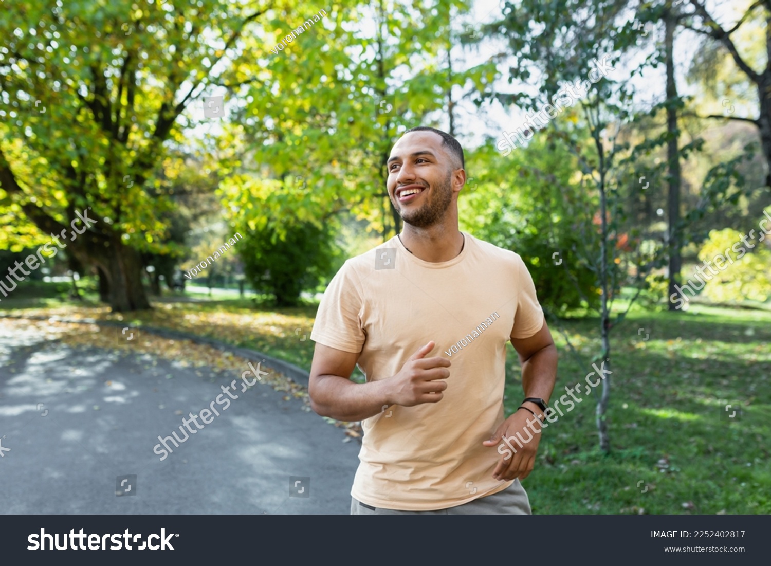 Cheerful and successful hispanic man jogging in the park, man running on a sunny day, smiling and happy having an outdoor activity. #2252402817