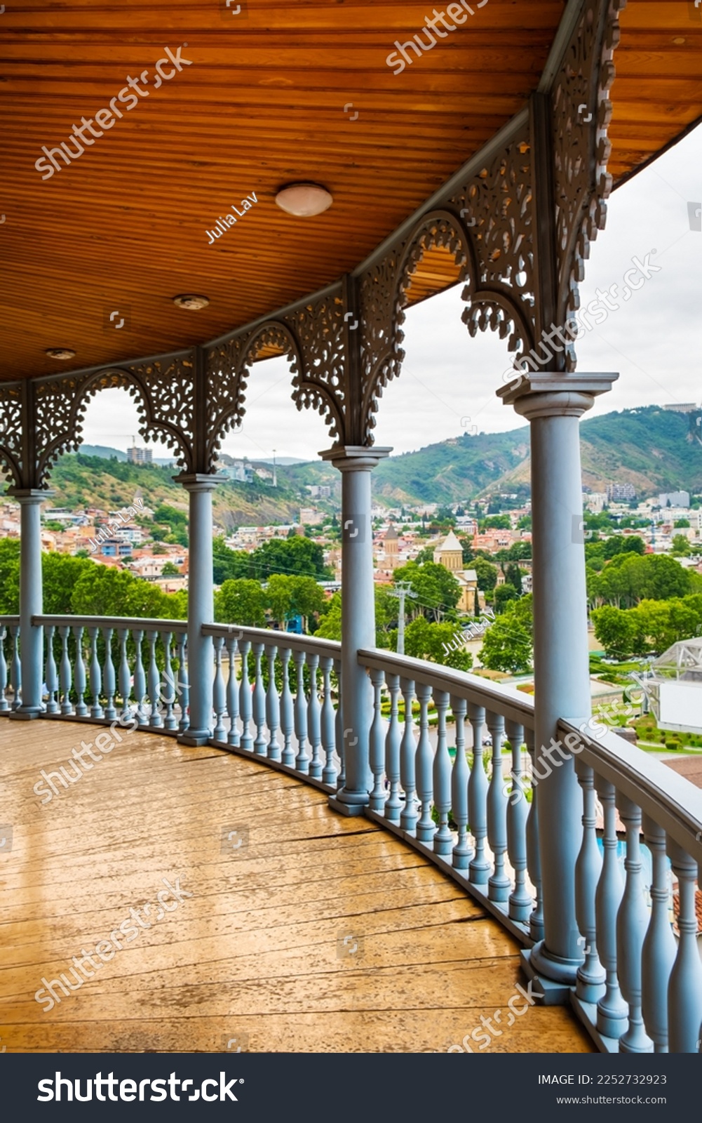 Carved wooden balcony with view to Rike park, hills and colorful buildings in historical Tbilisi, Georgia. Traditional decoration of Georgian house in Tiflis old town. Vertical orientation #2252732923