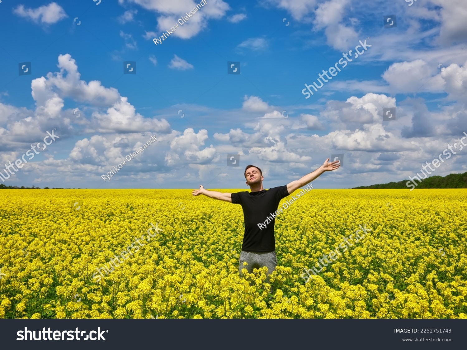 Attractive man with arms outstretched. Handsome young man standing in a field of blooming yellow rapeseed flowers. #2252751743