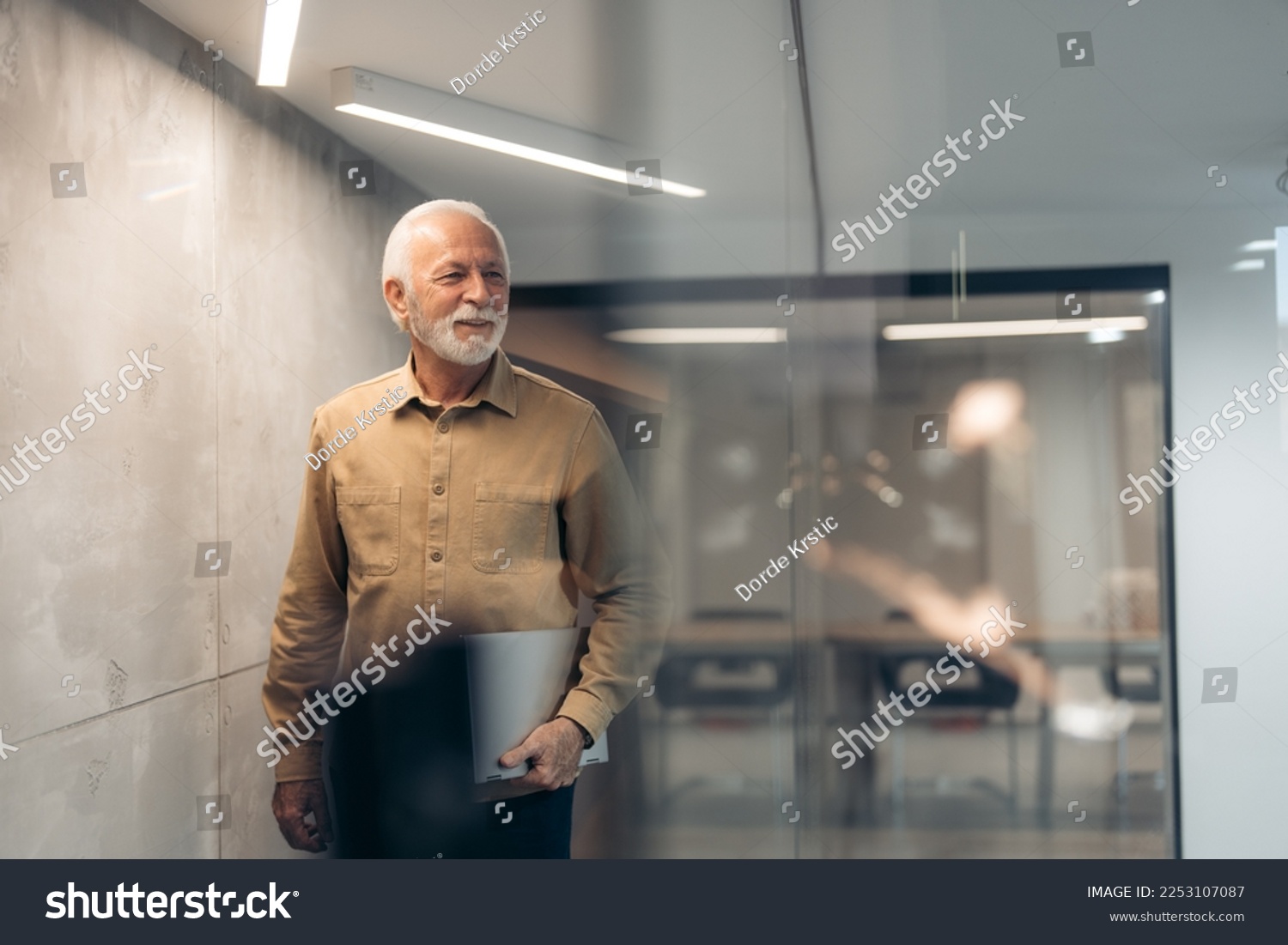 Smiling mature older successful gray-haired businessman leader, thoughtful senior professional businessman holding laptop looking away standing in modern office. #2253107087