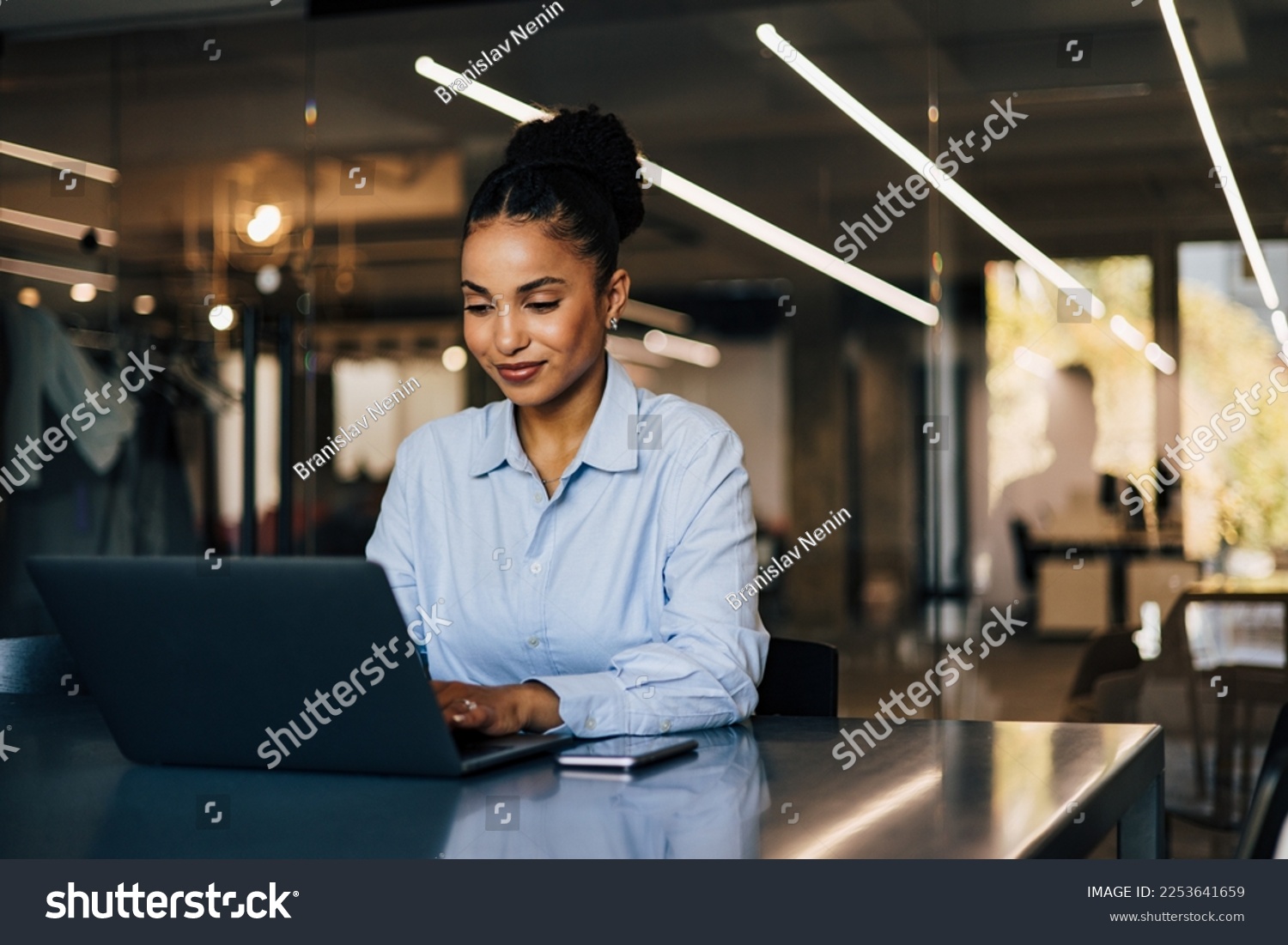 Positive African businesswoman sitting by the desk, typing something on the laptop. #2253641659