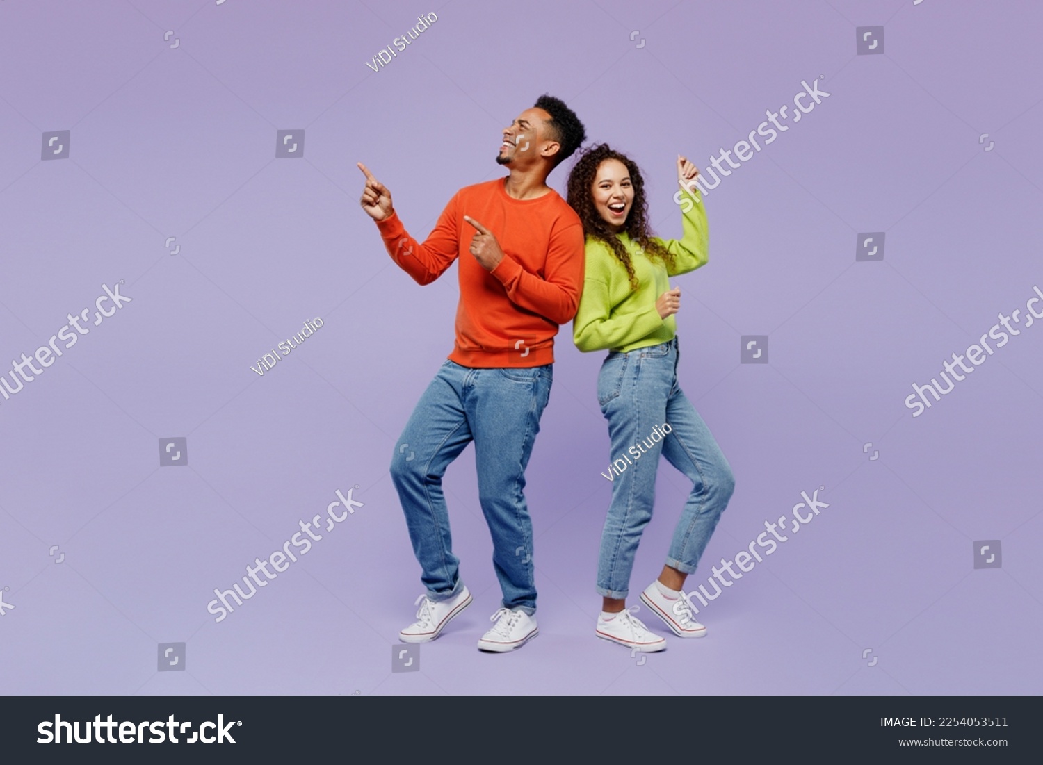 Full body sideways fun young couple two friends family man woman of African American ethnicity wear casual clothes together point finger aside on area isolated on pastel plain light purple background #2254053511