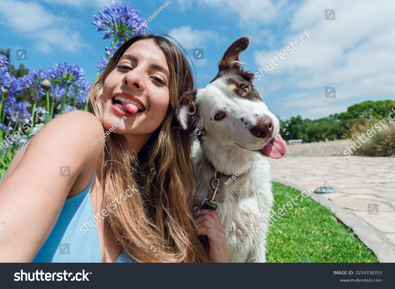 Selfie portrait of young Colombian Latina woman, with her border collie dog, in the park sticking out her tongue and looking at the camera, with the sky and trees in the background, phone perspective. #2254338353