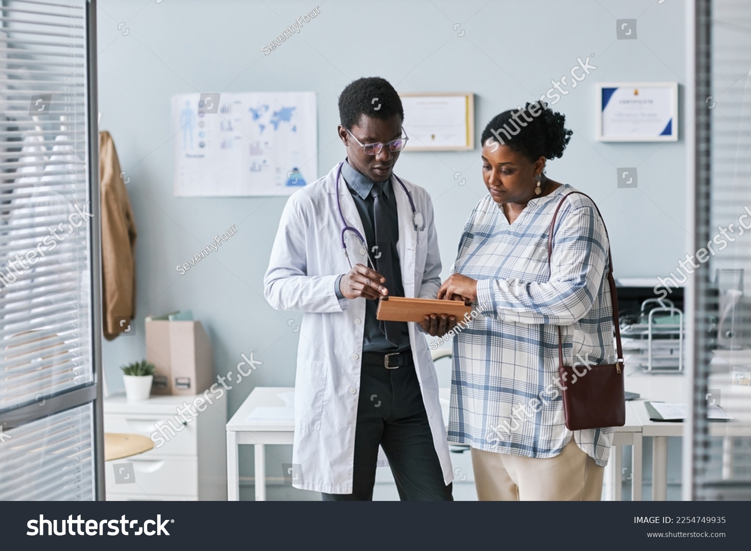 Waist up portrait of young African American doctor consulting female patient using digital tablet in clinic setting #2254749935