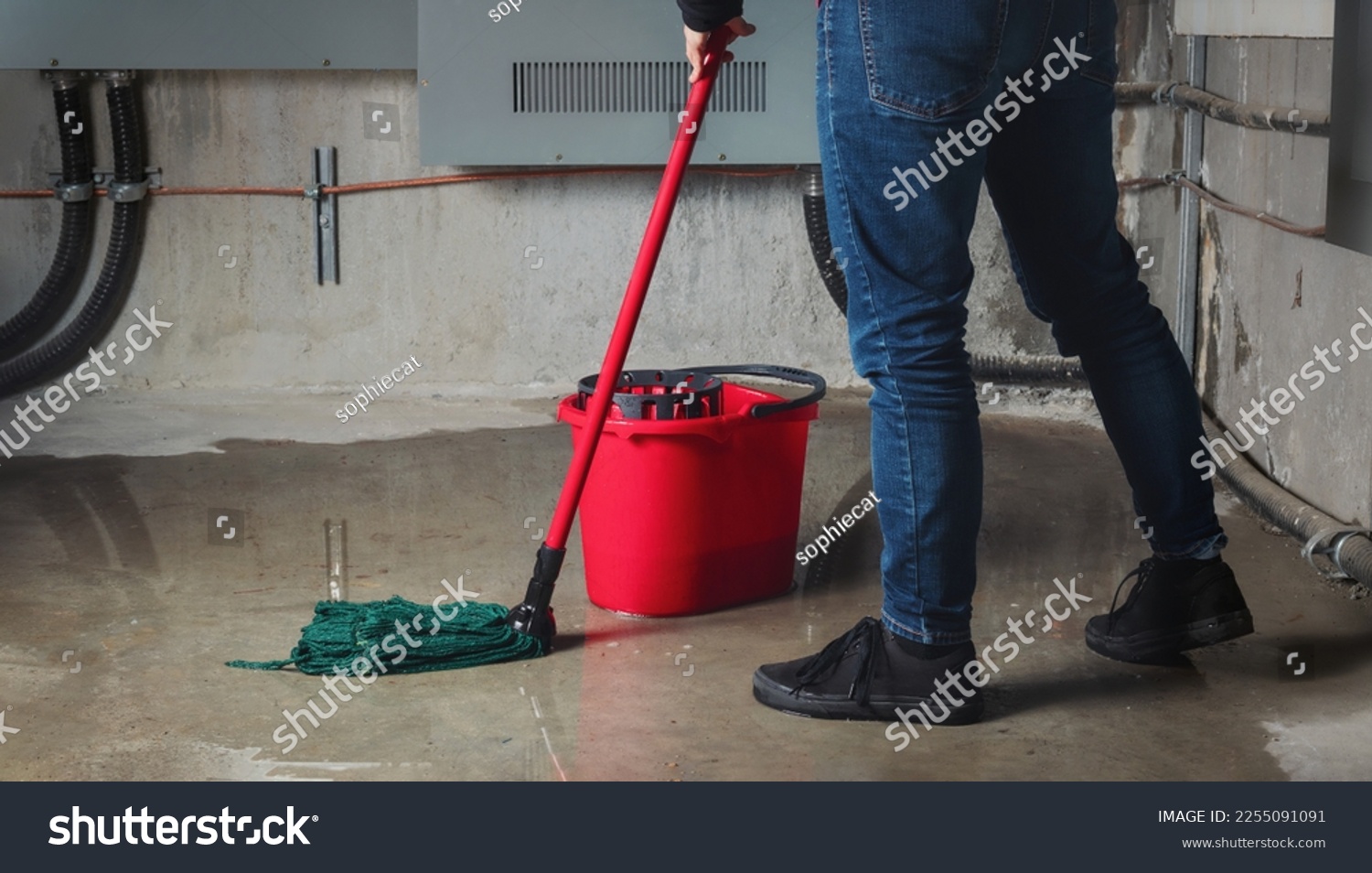 Woman mopping flood from water leaks in basement or electrical room. Water damage from rain, snowmelt or pipe burst coming from multiple cracks and leaks in concrete wall and ceiling. Selective focus. #2255091091