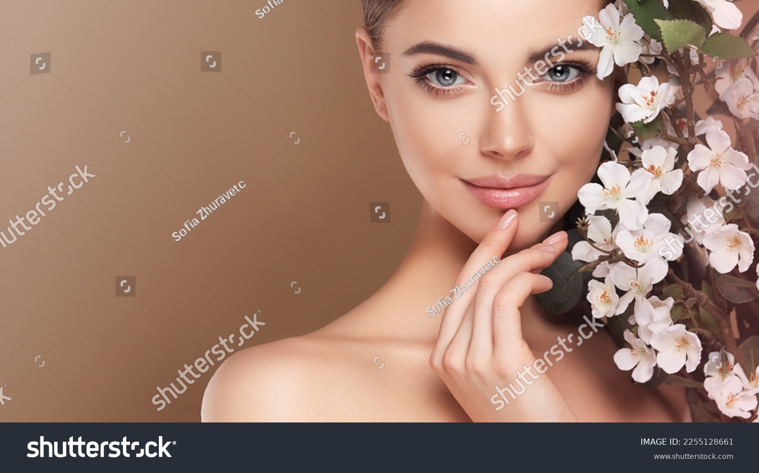 Beautiful young woman with clean fresh skin touching her face in flowers  . Girl facial  treatment   . Cosmetology , beauty  and spa . Female  model, care concept  #2255128661