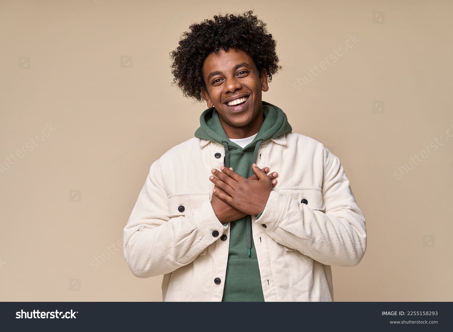 Happy pleased excited grateful African American teen guy holding hands on chest expressing gratitude, feeling trust hope love in heart, impressed with kindness isolated on beige background. #2255158293