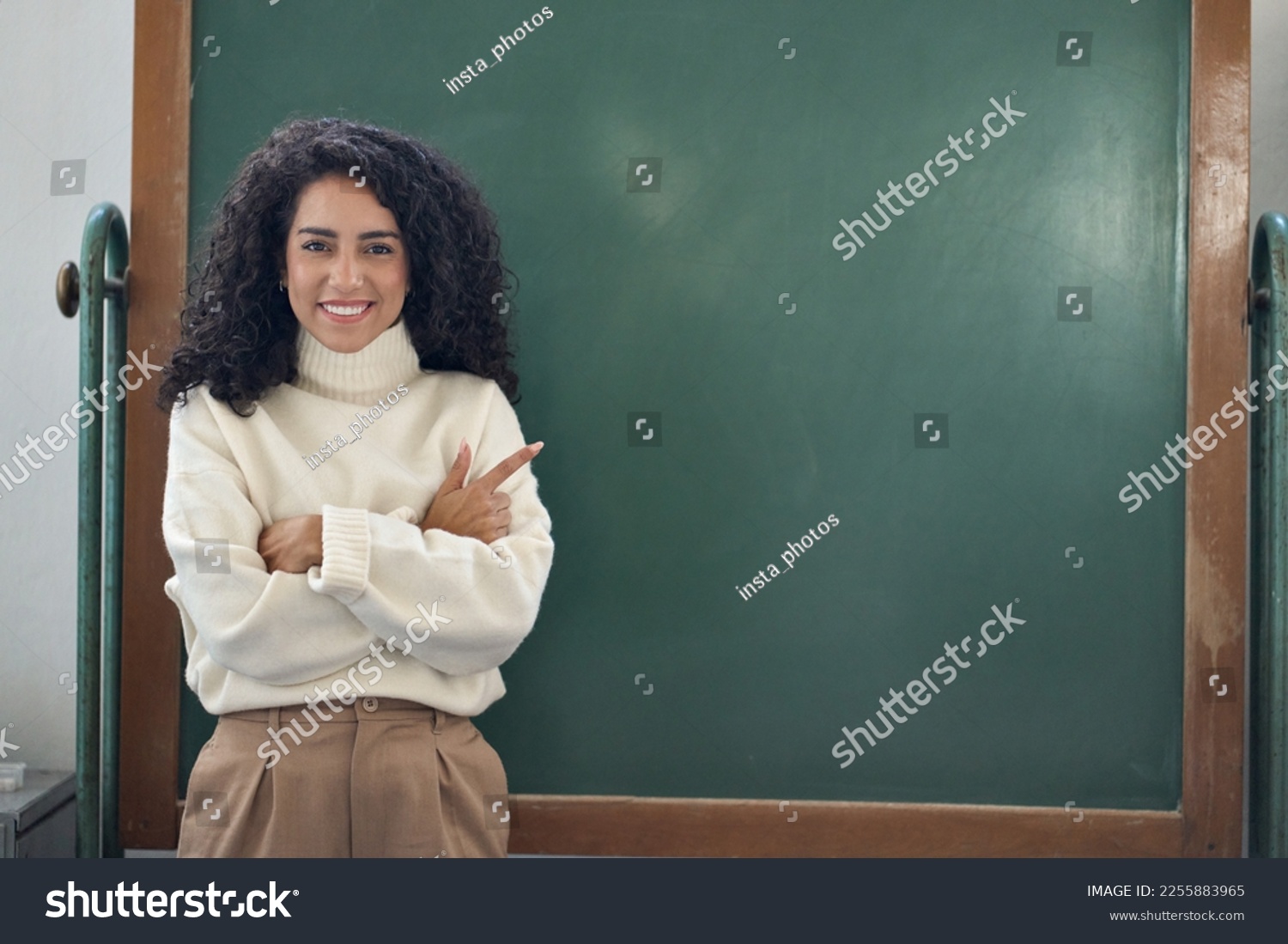 Young happy woman school professional teacher, female coach leader pointing at empty blank mock up chalkboard in classroom presenting showing business training course virtual education classes ads. #2255883965