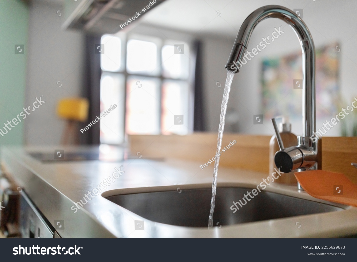 Close up shot of modern kitchen faucet with water running from tap, flow falling to empty dish sink at stylish home interior, selective focus, sustainable resources consumption concept #2256629873