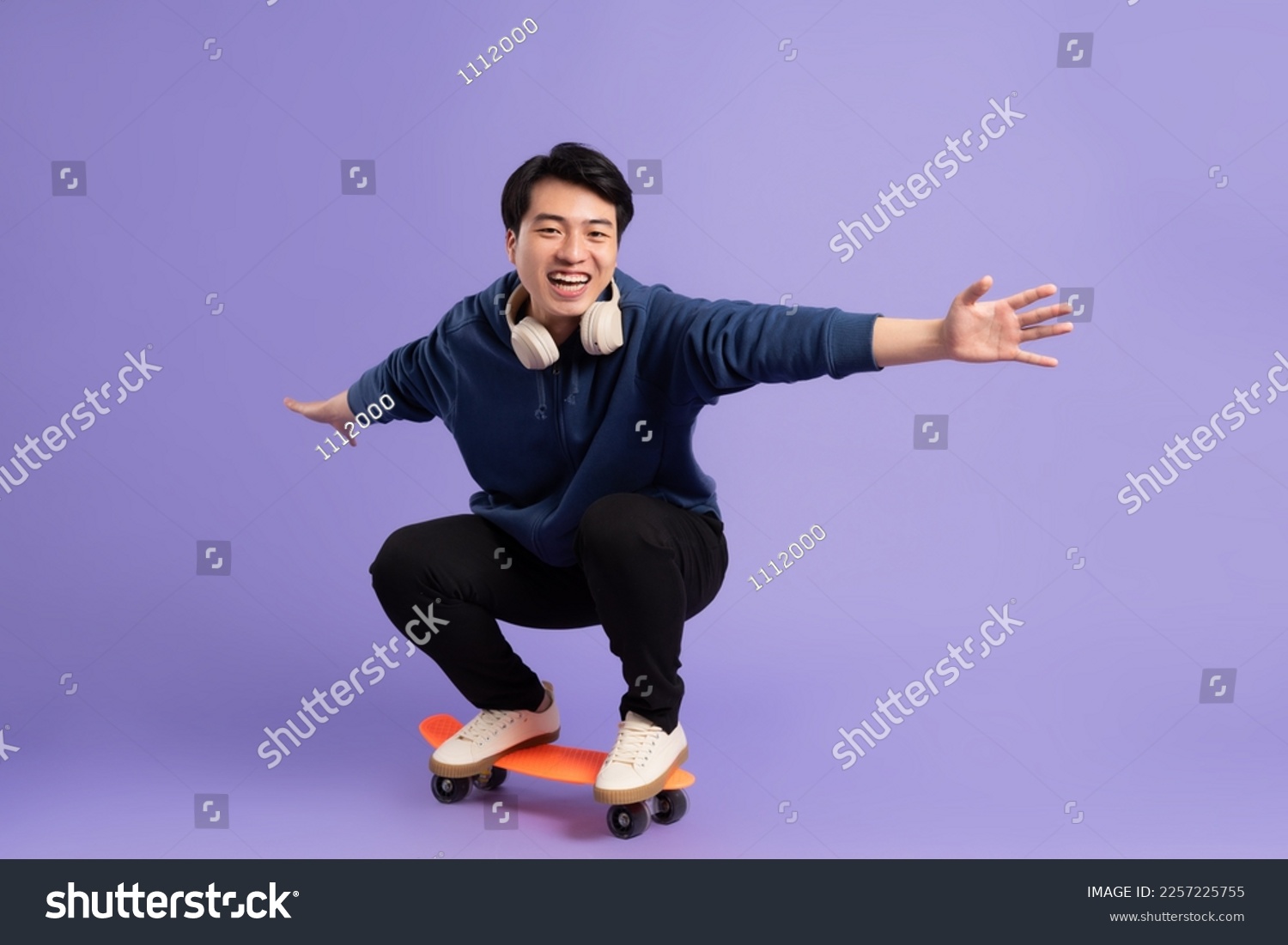 Image of young Asian man playing skateboard on purple background #2257225755