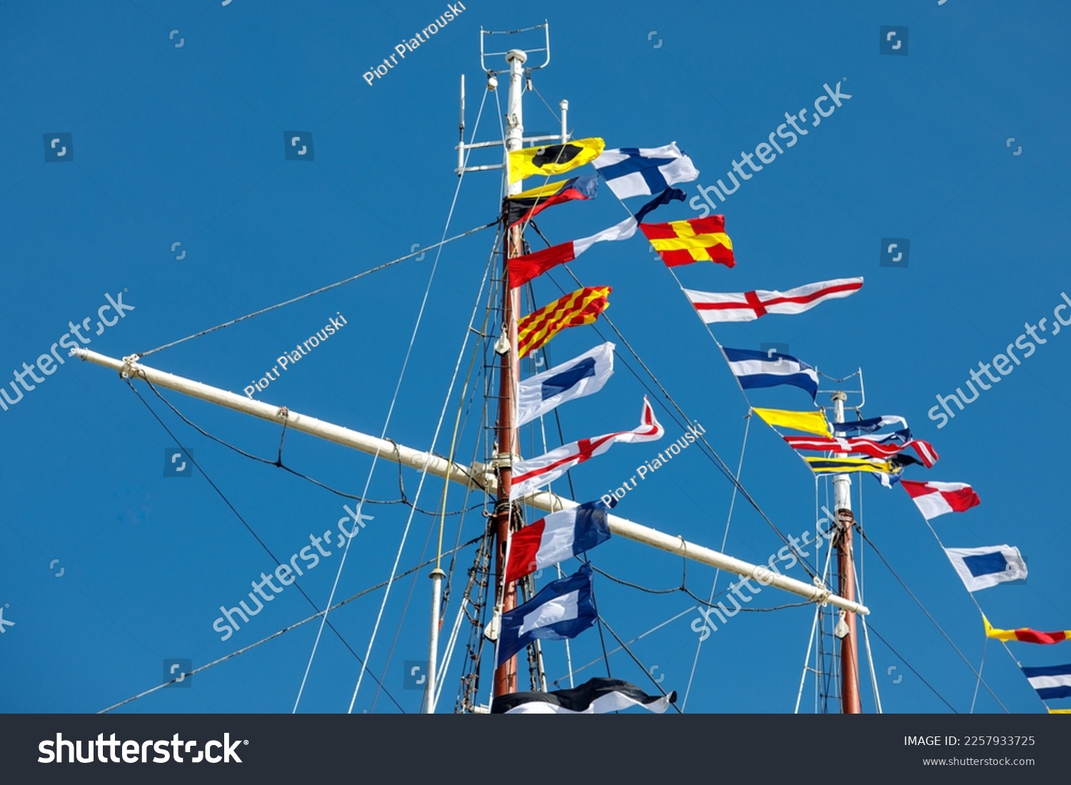 International maritime signal flags on a flagpole and masts on a sailing ship with a blue sky in the background #2257933725