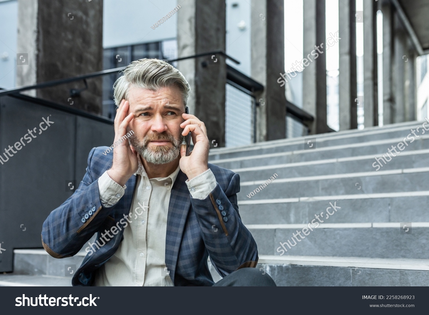 Upset and disappointed mature businessman sitting on stairs of office building outside, man in business suit bankrupt talking on the phone, senior boss investor lost money #2258268923