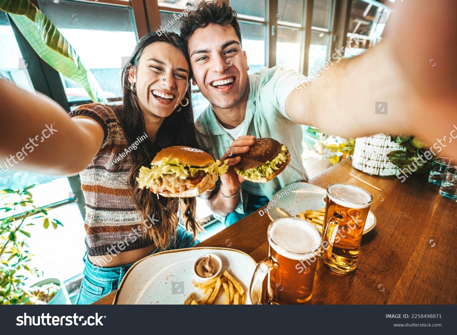 Happy couple taking selfie with smart mobile phone at burger pub restaurant - Young people having lunch break at cafe bar venue - Life style concept with guy and girl hanging out on weekend day  #2258498871