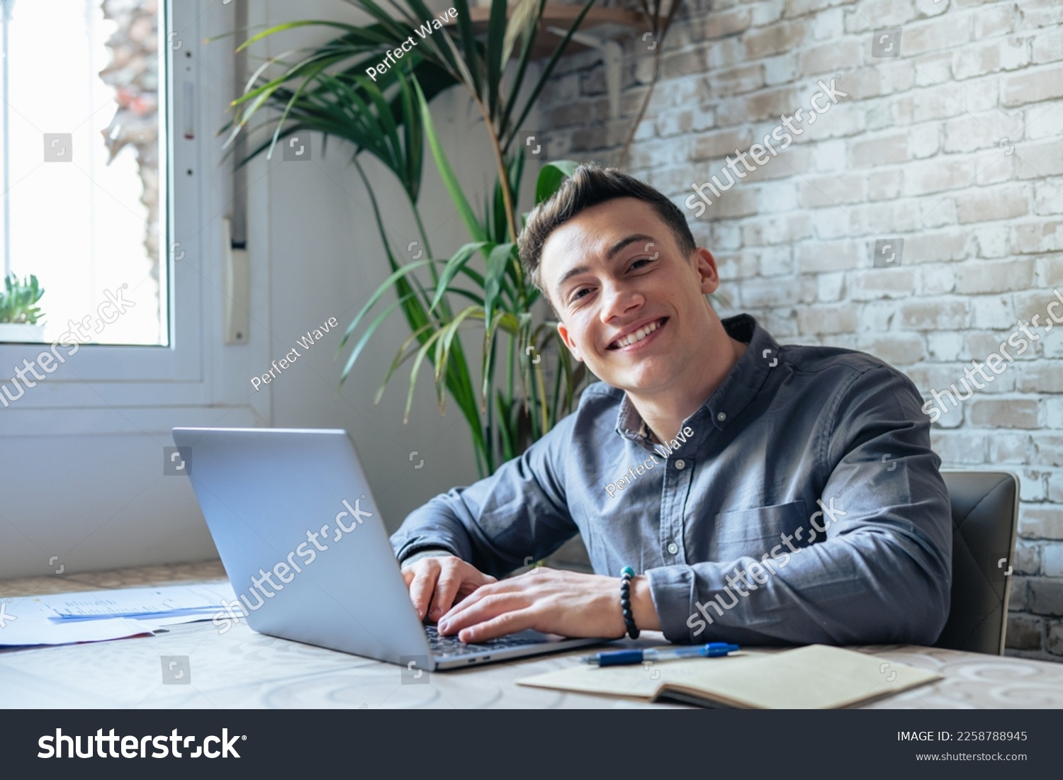 Good-looking millennial office employee in glasses sitting at desk in front of laptop smiling looking at camera. Successful worker, career advance and opportunity, owner of prosperous business concept #2258788945