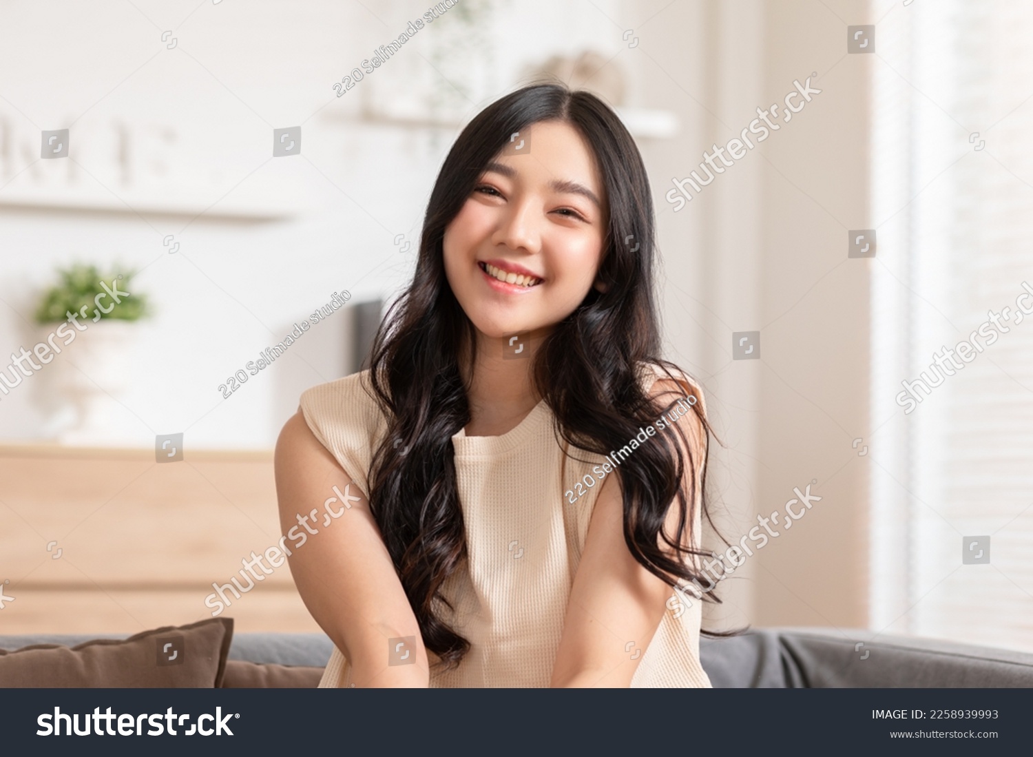 Stunning Beautiful Attractive Asian young woman sit on couch or sofa looking at camera and smile happiness and comfortable at home.Cute girl smile cross arm confident and relax in living room #2258939993