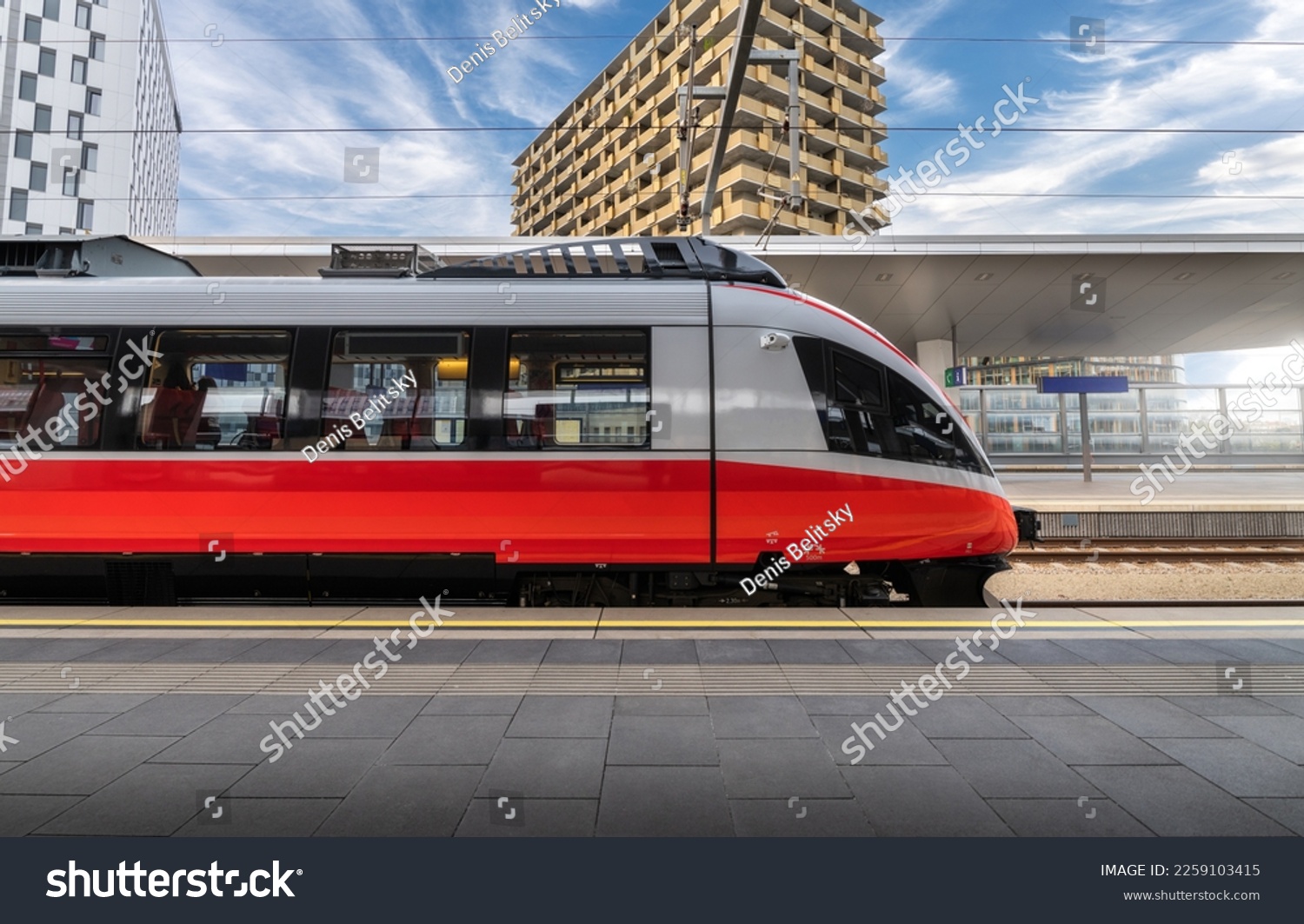 High speed train on the train station at sunset in Vienna, Austria. Beautiful red modern intercity passenger train on the railway platform, buildings. Side view. Railroad. Commercial transportation #2259103415