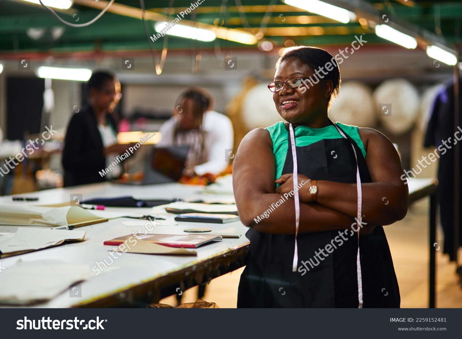 african female business woman textile industry wearing a green shirt with black apron measuring tape with arms folded #2259152481