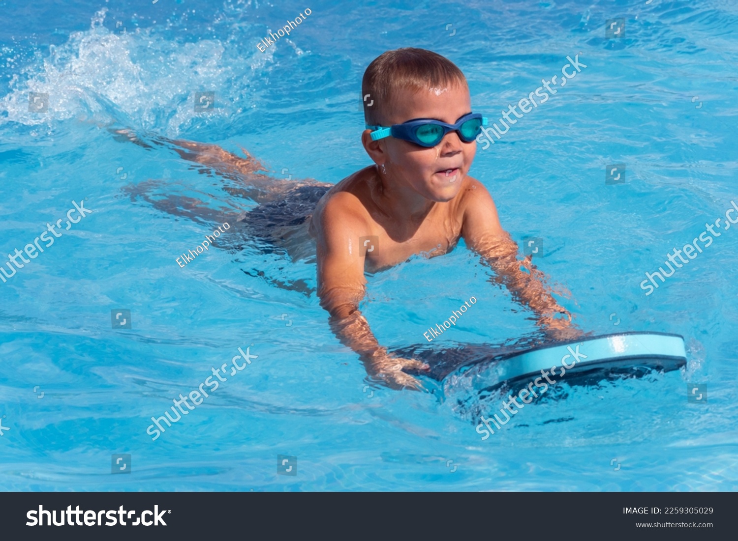 Happy boy child in swimming goggles with float foam board tool swim in pool in sunny day. Safe pool training, summer holiday, family vacation, travel, water sport concept #2259305029