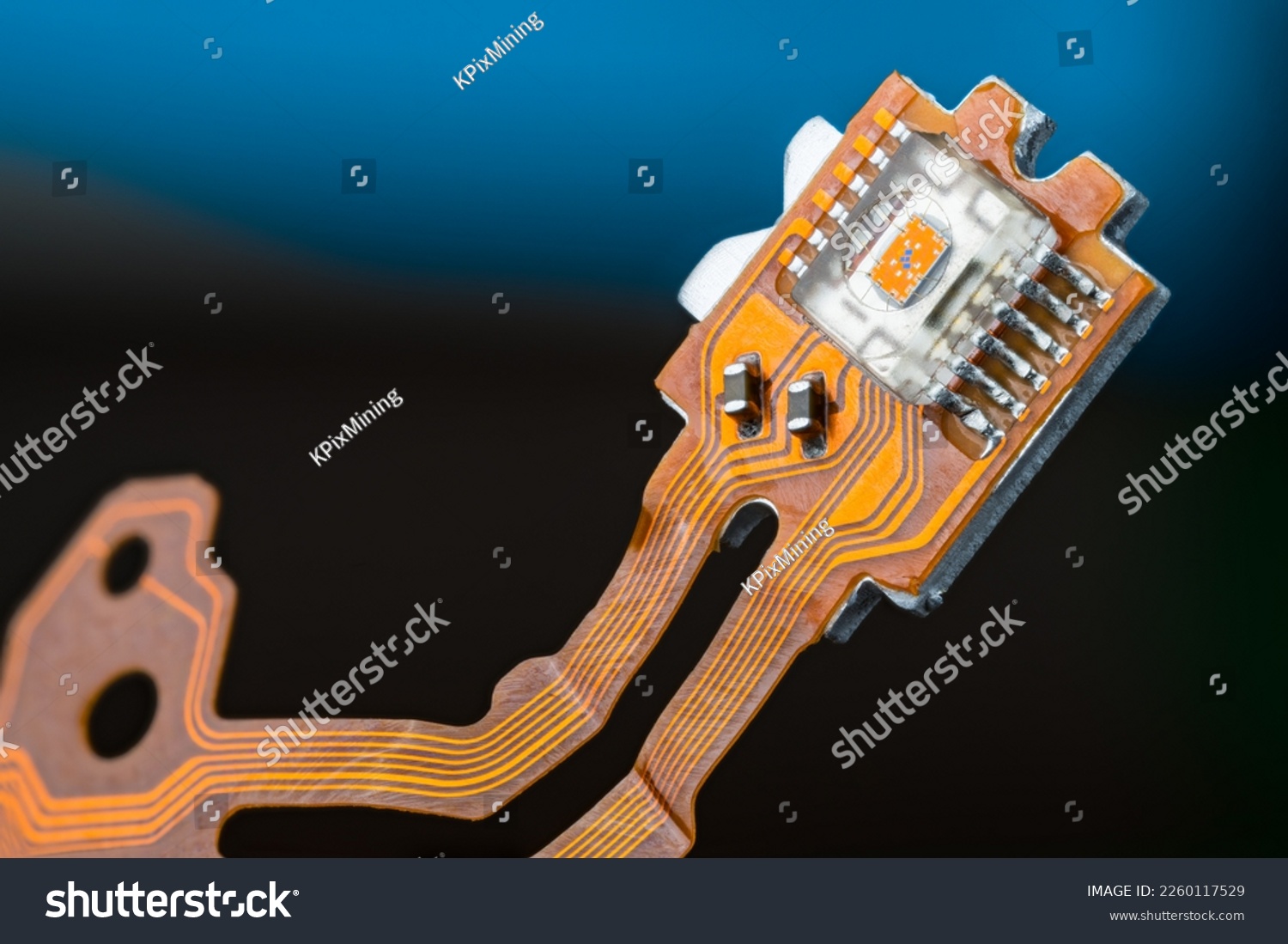 Closeup of optical sensor on electronic printed circuit board and flex ribbon cables on dark blue background. Small orange die in transparent micro chip on PCB of dismantled digital CD-DVD disc drive. #2260117529