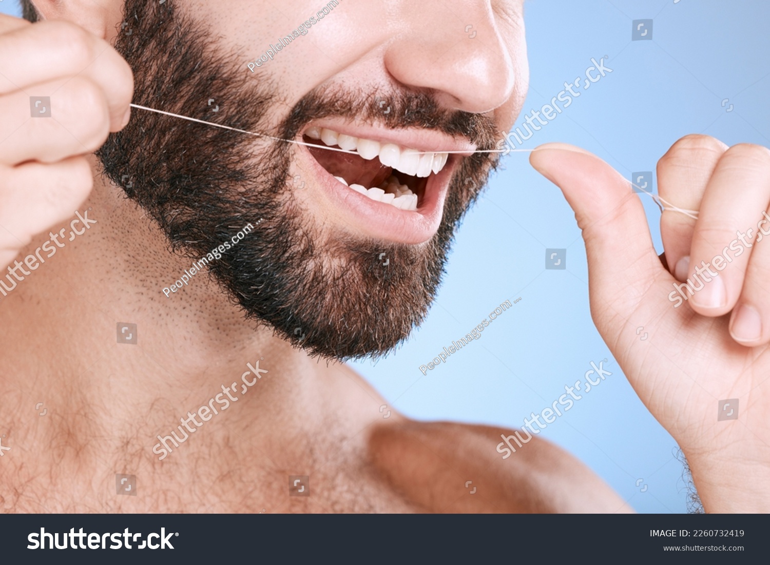 Dental, floss and oral hygiene with a man in studio on a blue background cleaning his teeth for healthy gums. Dentist, healthcare and mouth with a young male flossing to remove plague or gingivitis #2260732419
