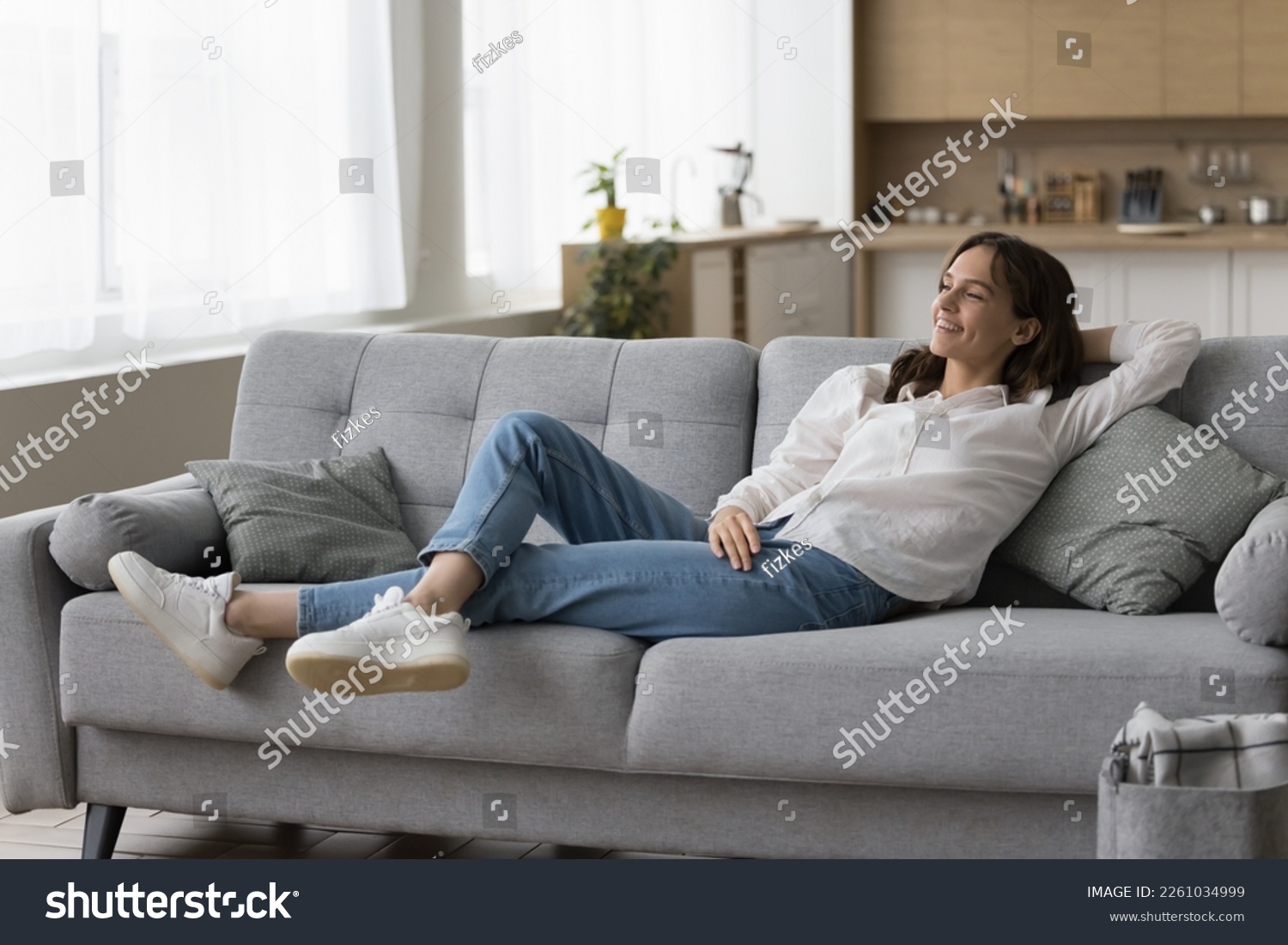 Positive peaceful young woman resting on sofa at home, leaning on back, breathing fresh air, looking at window away, enjoying break, leisure, thinking, dreaming. Full length shot #2261034999