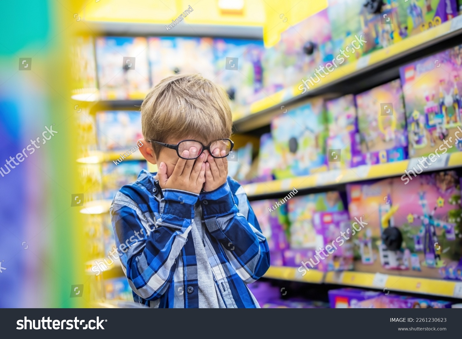 The little boy in the toy store is upset. The kid covered his eyes with his hands, crying. Child's tears in toy shop.  #2261230623