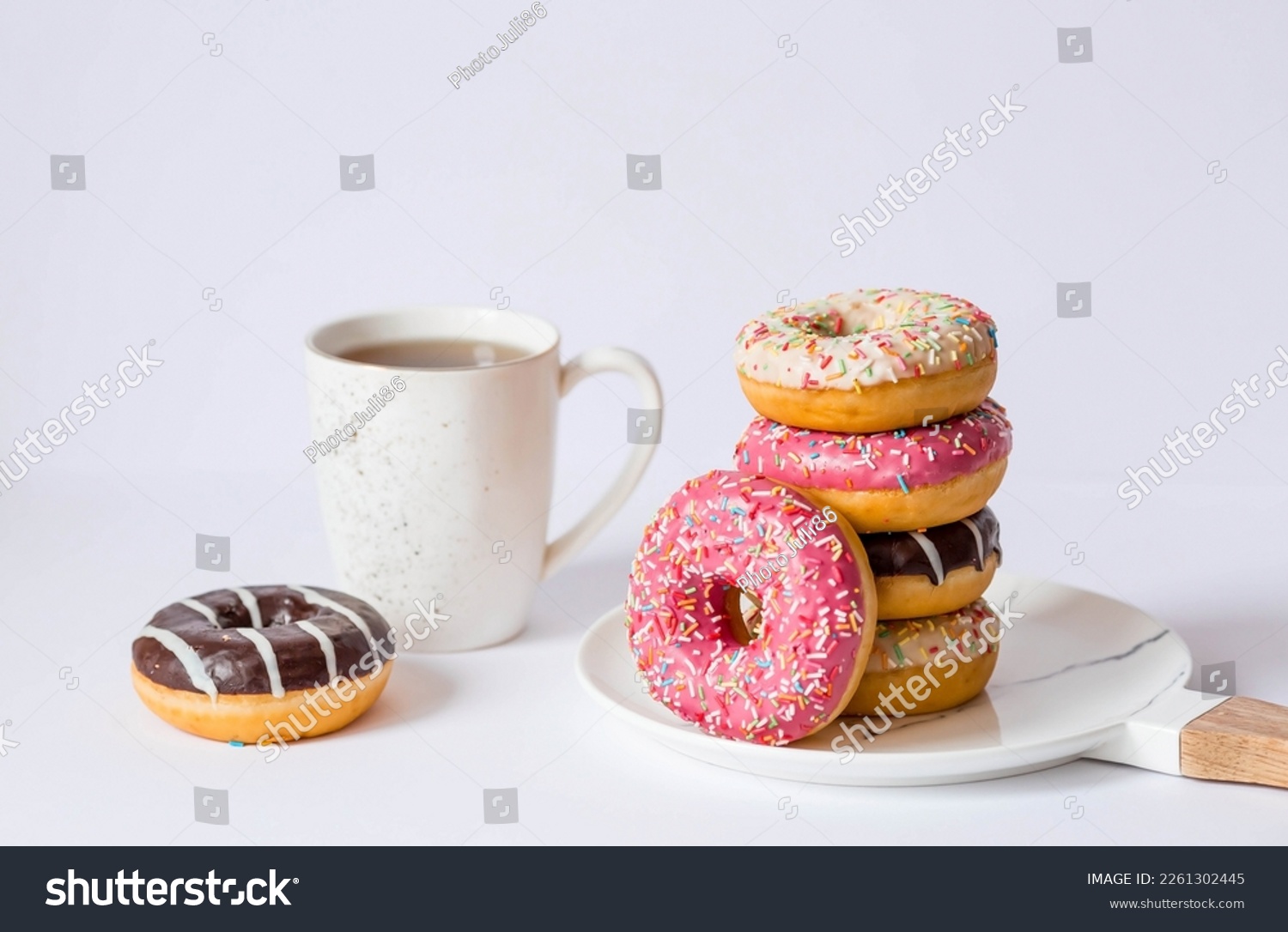 Delicious dessert. Pink, white and chocolate donuts with multicolored sprinkles, a cup of black coffee or tea. Sweets. #2261302445